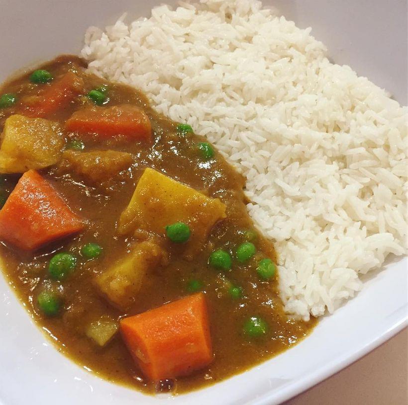 Carrots, peas, and potatoes in a pool of brown curry sauce, served on a bed of white rice.