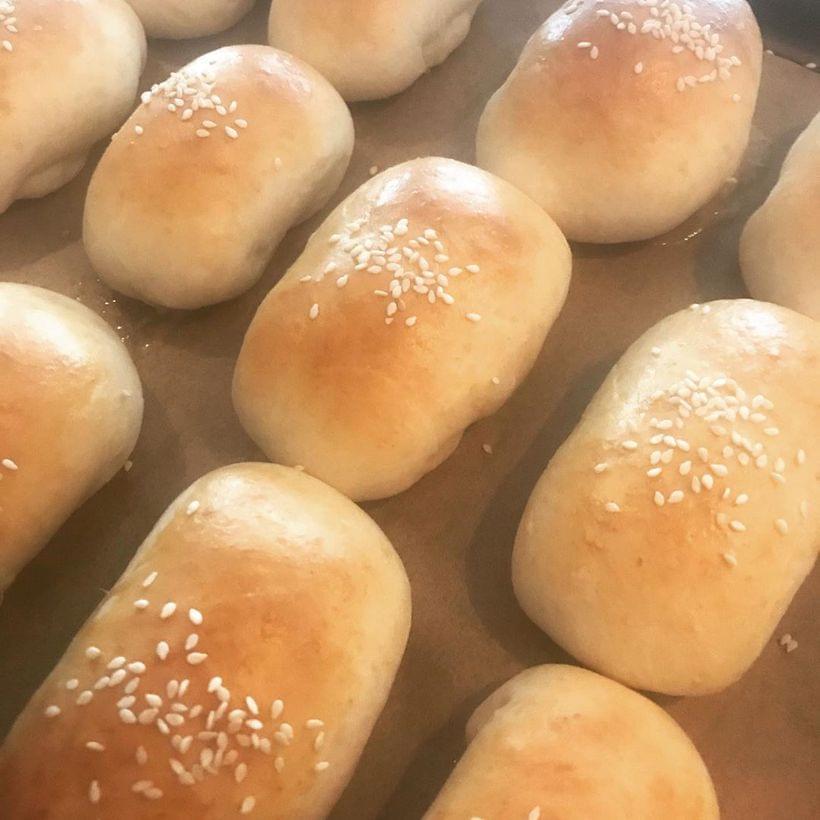 Three rows of golden brown baked bao, speckled with white sesame seeds, on a parchment-lined baking sheet.