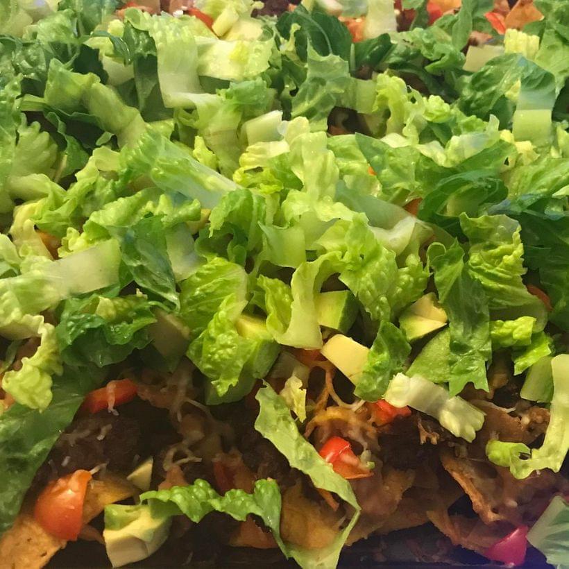A close-up of a tray of nachos, piled—perhaps to excess—with meat, beans, lettuce, tomatoes, and red peppers.
