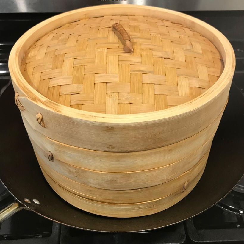A wok on a stovetop, containing a stack of bamboo steamer baskets.