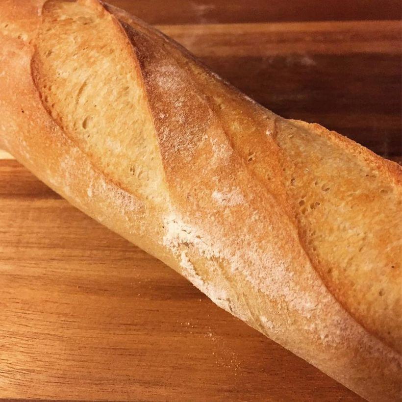 A close-up of a baked baguette with wide, almond-shaped gaps in the crust.