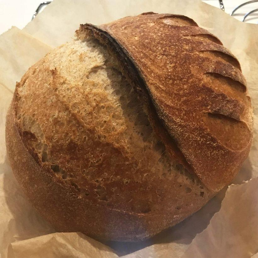 A rich, reddish-brown sourdough boule with a blistered crust and a wide “grigne”—a slash down the center, split open by the bread rising in the oven.