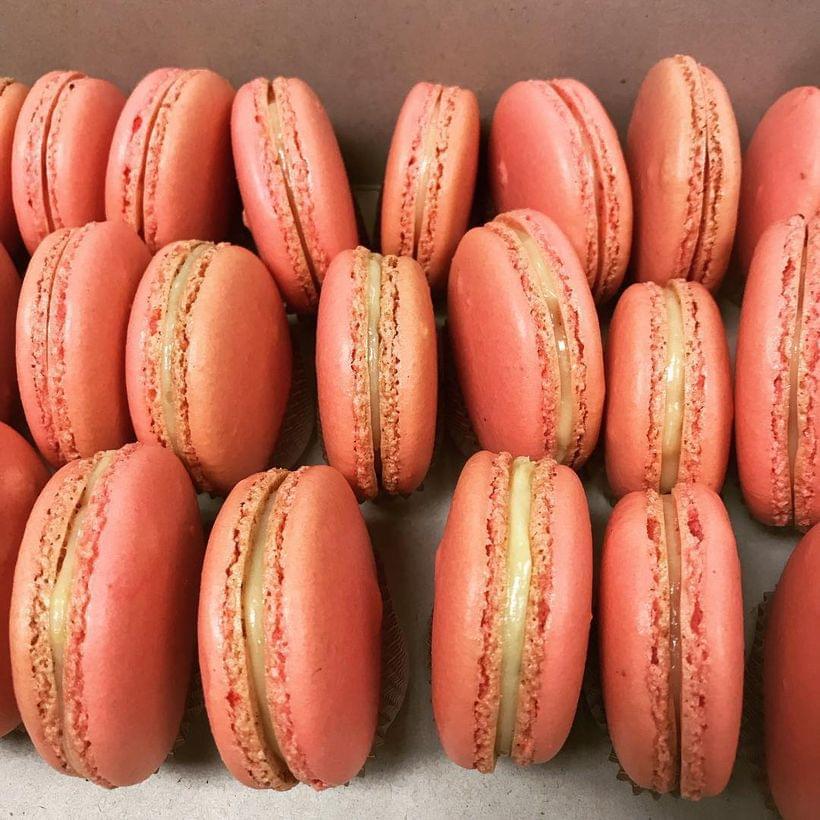 Rows of pink macaron shells filled with a pale yellow ganache.