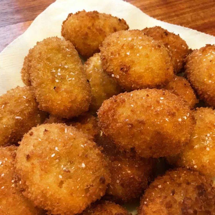 A pile of golden brown croquettes, dusted with salt.