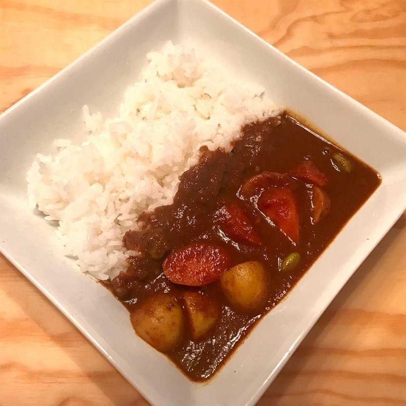 Carrots and potatoes in a pool of dark brown curry sauce, served on a bed of white rice.
