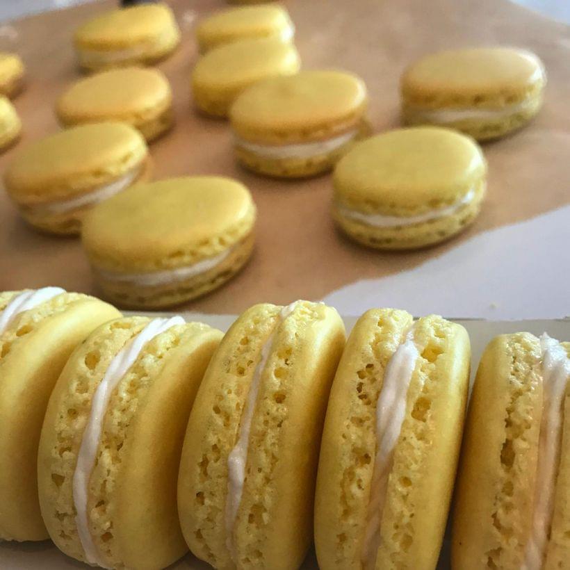 Bright yellow macarons with white buttercream filling, on a sheet of parchment paper.