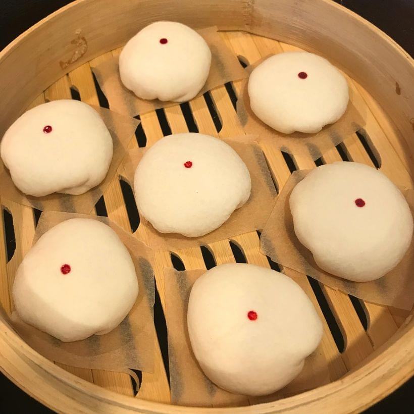 A handful of small, round, white dumplings, each with single red dot on the top, inside of a bamboo steamer basket.