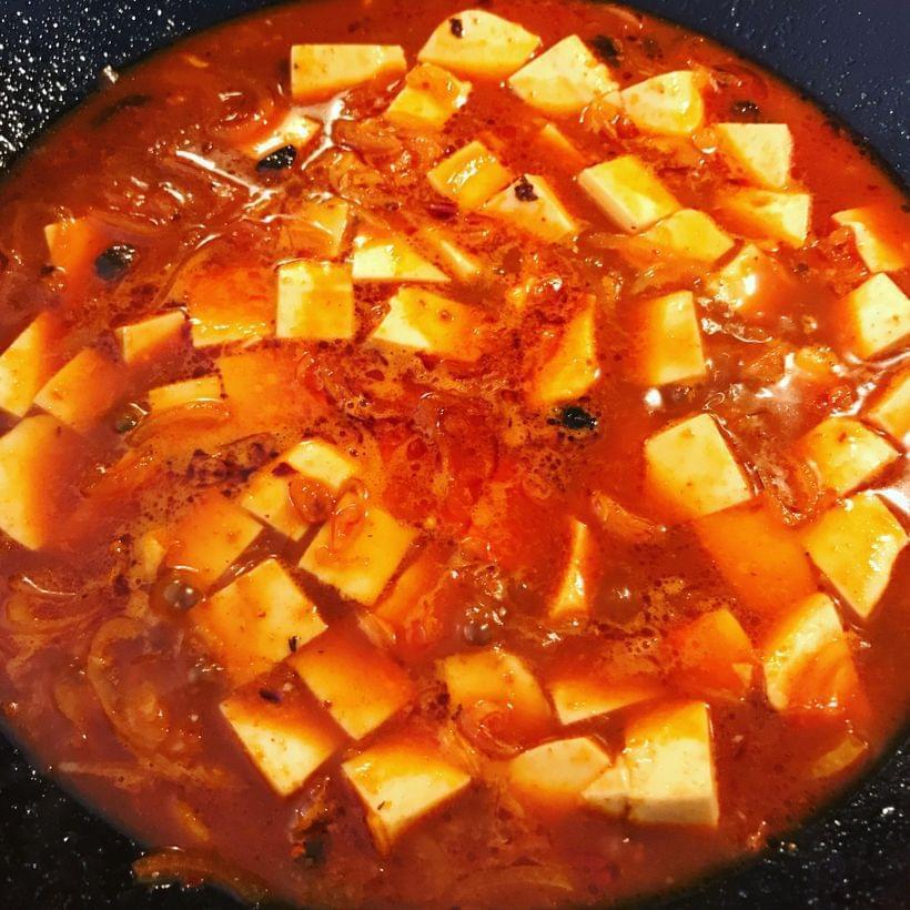 A wok containing cubes of tofu simmering in a fiery red sauce.