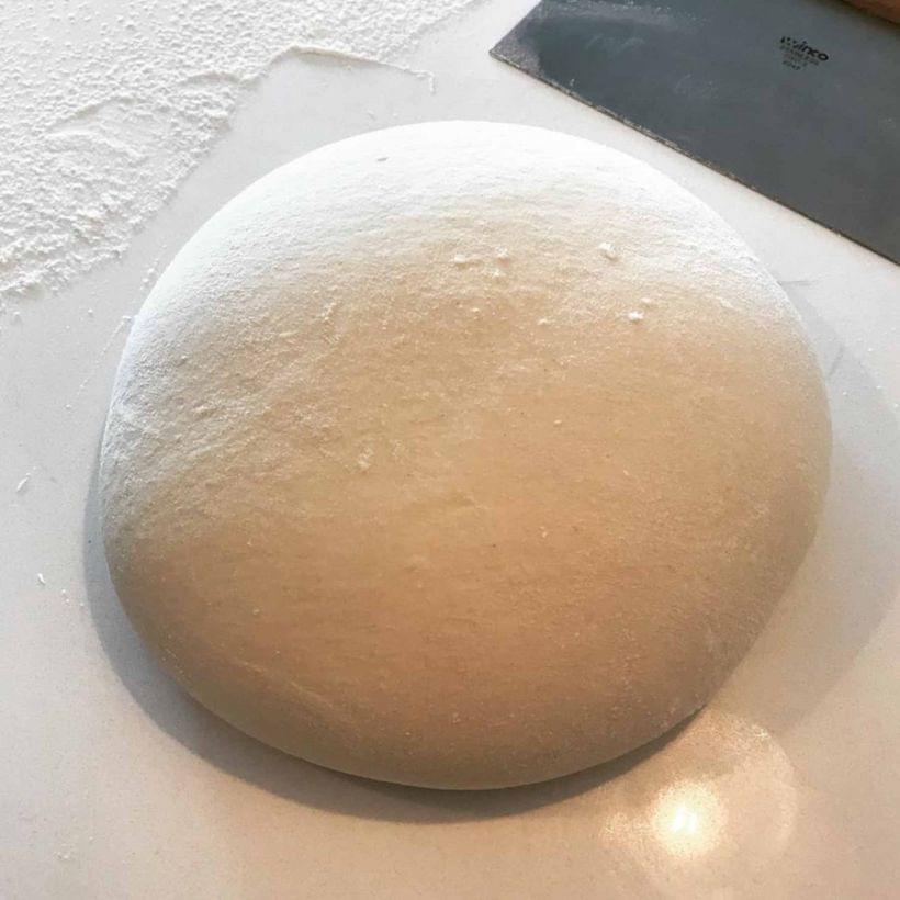 A ball of pale dough resting on a floured countertop.