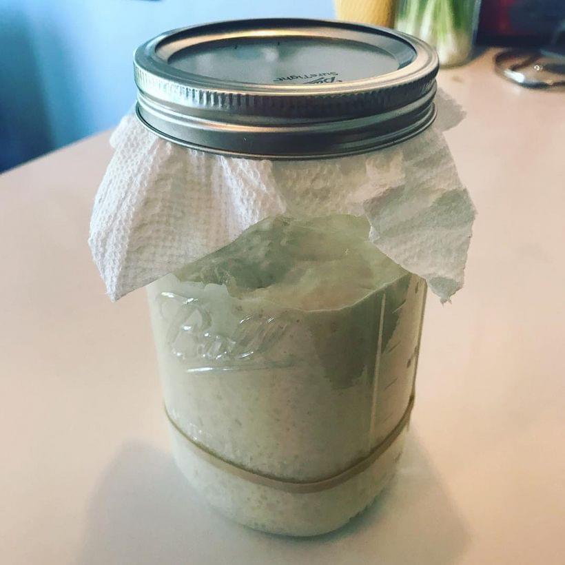 A mason jar 75% full of bubbling sourdough starter. A rubber band marks the initial size of the starter—about 25% full.