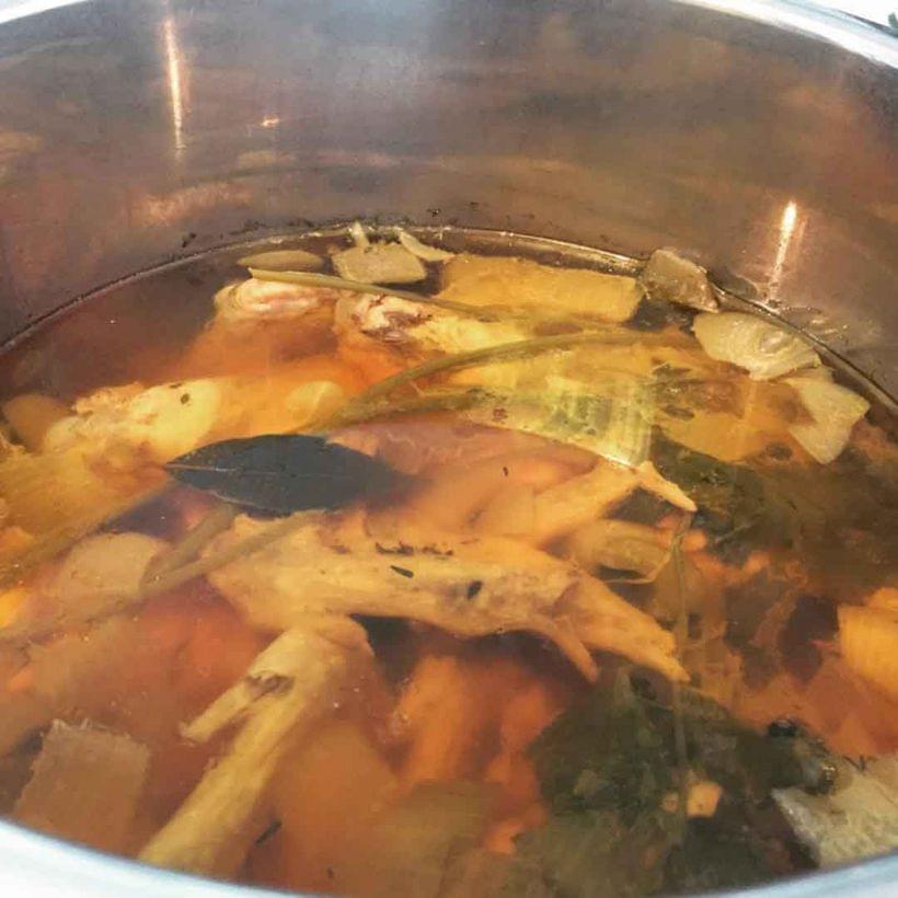 An open pressure cooker, containing herbs and chicken wings covered by water.