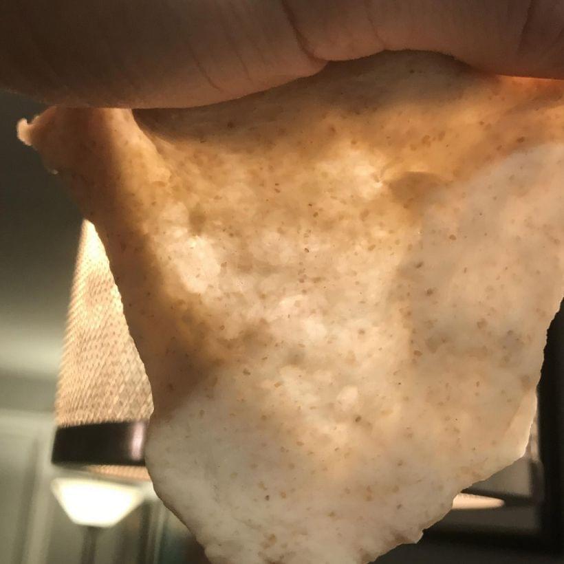 A small wad of dough, stretched thin, held up to a hanging lamp. Light is visible through the center of the dough.